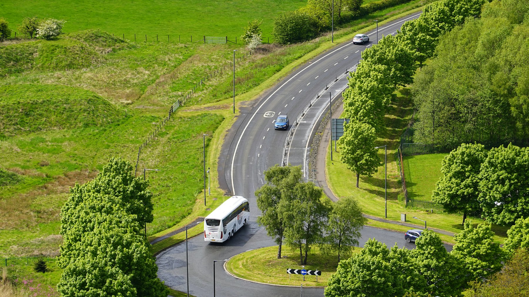 Ônibus de turismo em estrada cercada por área verde, vista aérea