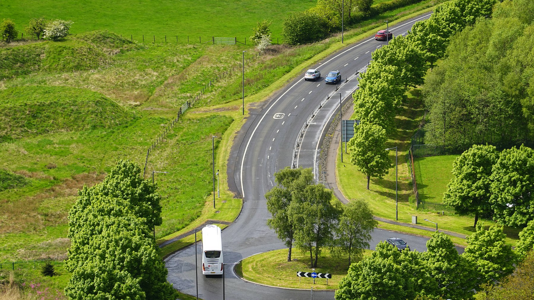 Ônibus de turismo percorrendo estrada em área verde, vista aérea